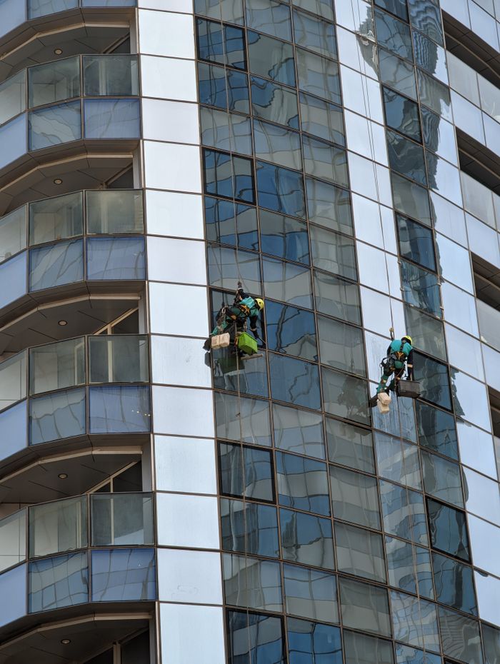 project-03-b Des nettoyeurs de vitres professionnels à l'œuvre sur un gratte-ciel à Abu Dhabi, mettant en valeur l'architecture urbaine.