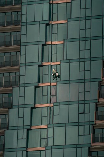 project-01-c Deux ouvriers nettoient les vitres d'une façade moderne en verre à l'aide d'une plateforme suspendue.